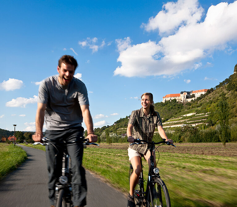 Zwei Personen fahren mit dem Fahrrad durch eine Landschaft.