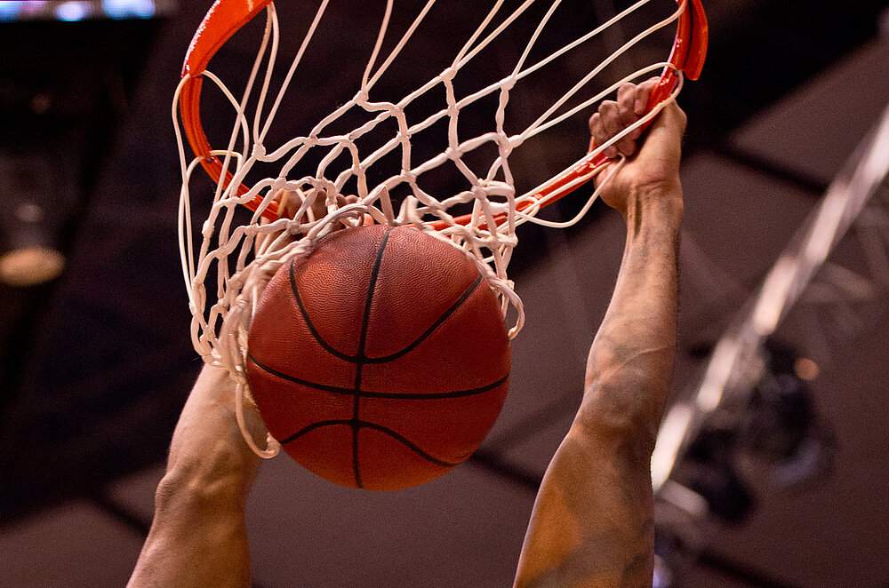 Basketball fällt durch Basketballkorb. Hände greifen an Basketballkorb